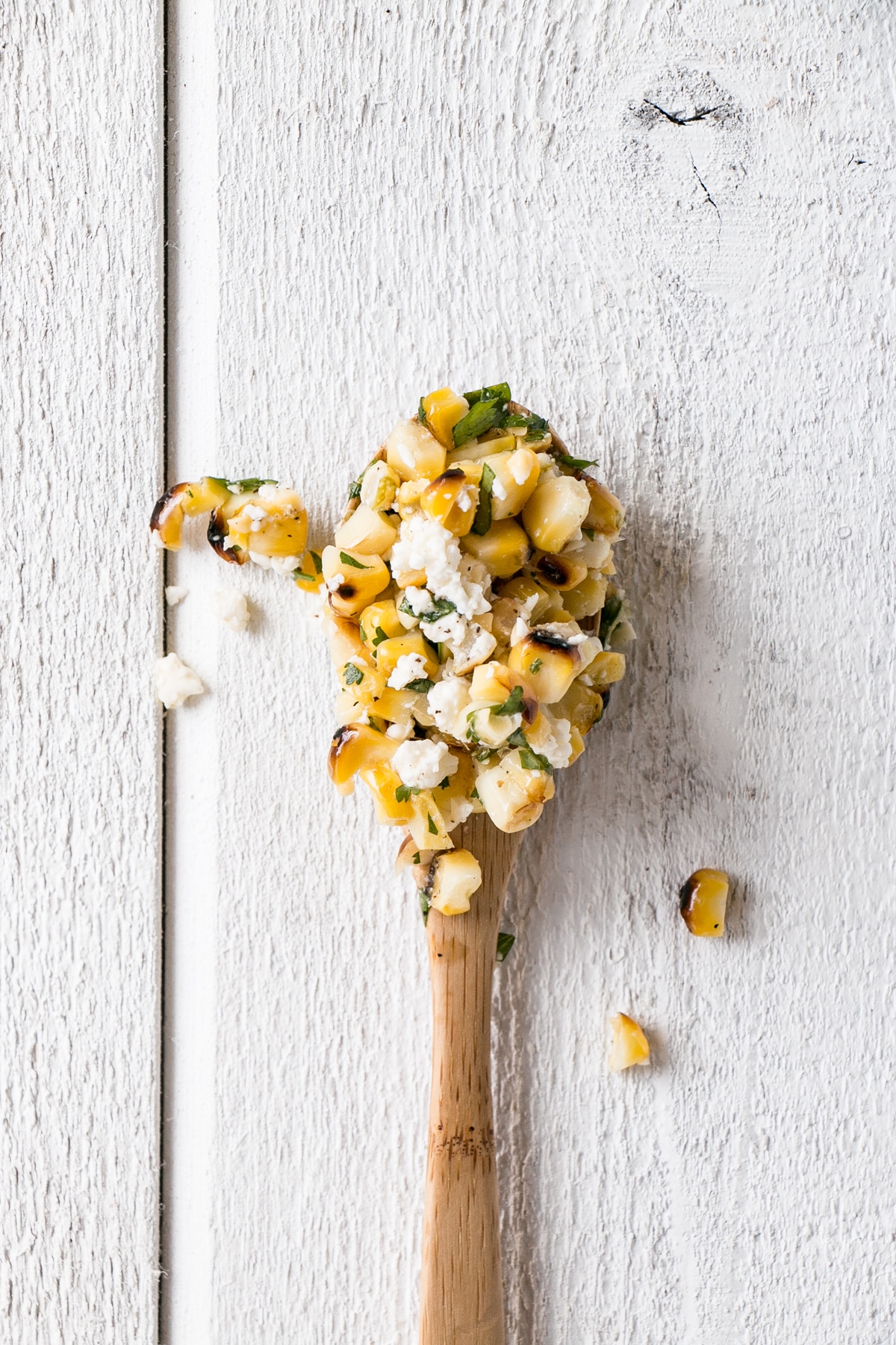 Grilled Corn and Avocado Salad on a wooden spoon with a white background.