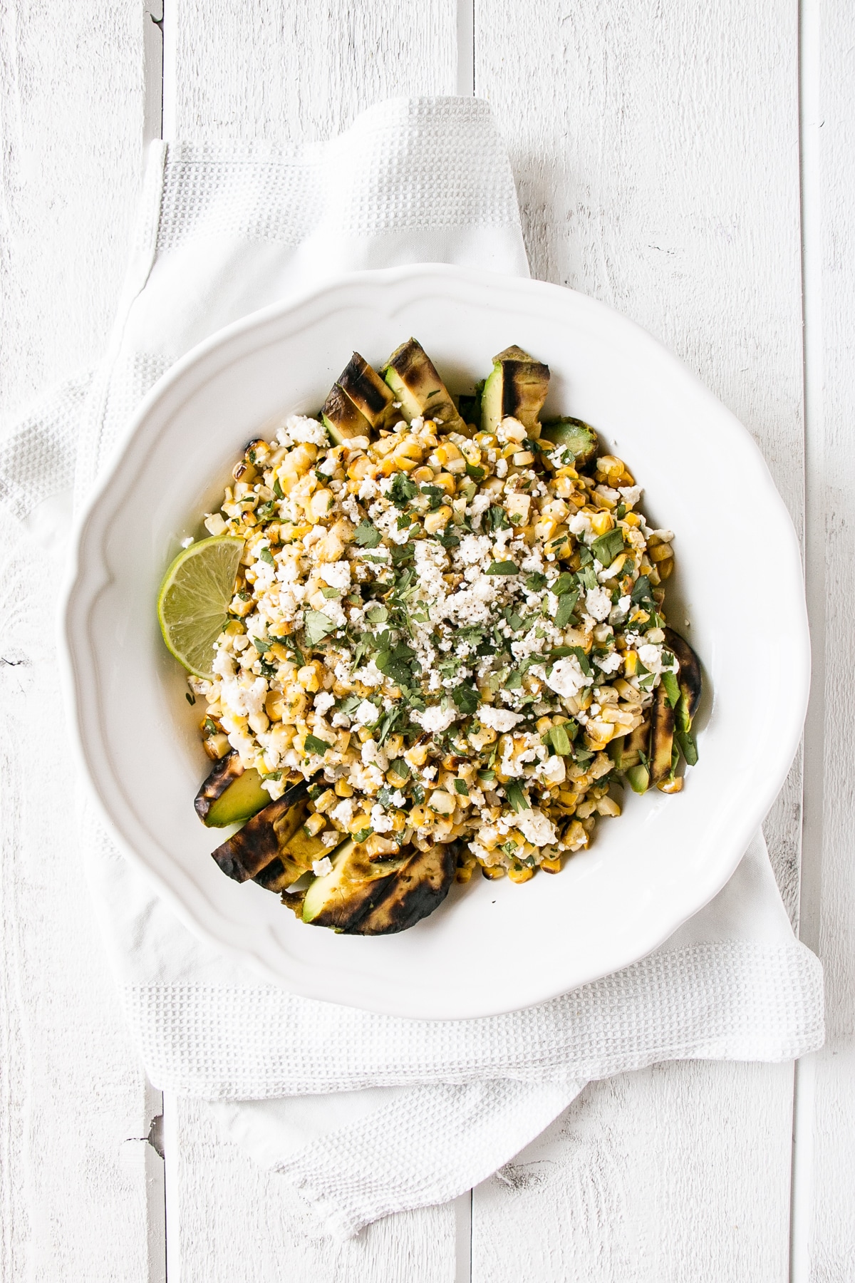 Grilled Corn and Avocado Salad with cilantro and feta cheese in a white serving bowl. 