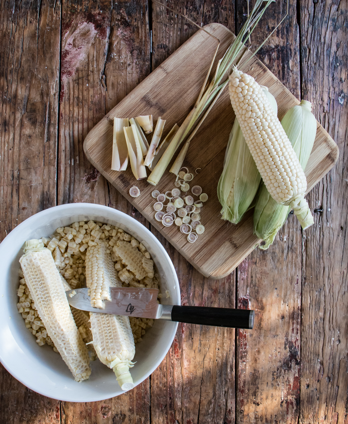 Kernels being removed from ears of corn in a white bowl