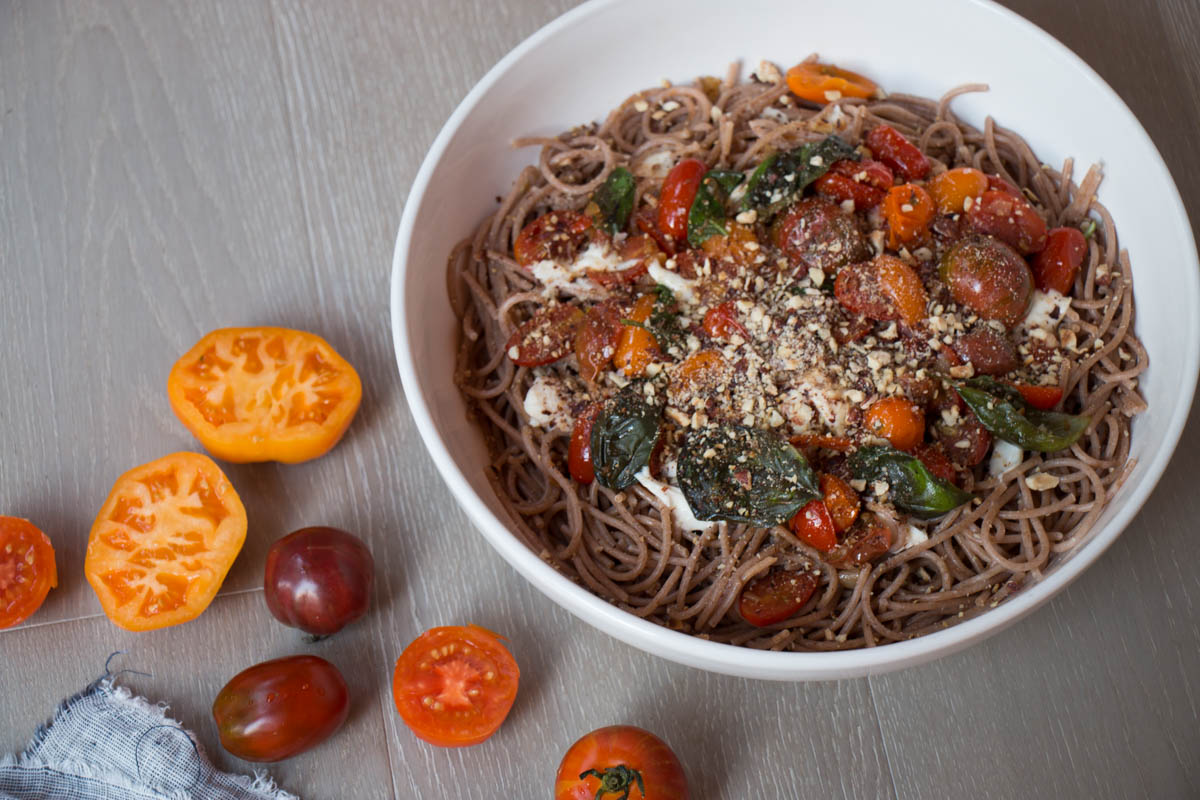 spaghetti with tomatoes and hazelnuts in a bowl with tomatoes beside it.
