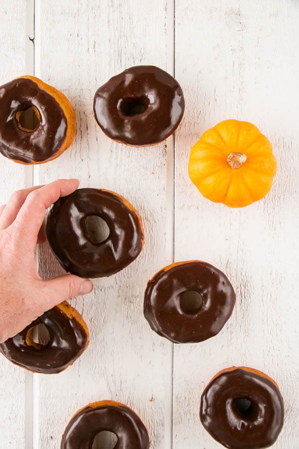 A hand reaching and about to pick up a Pumpkin Spice Donuts with Chocolate Glaze