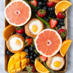 Oven Baked Eggs in buns on a baking tray with bright vibrant fruit and bright green asparagus.