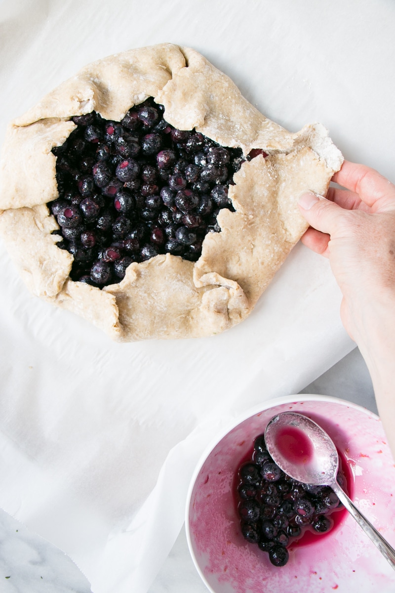 Blueberry Galette with a hand folding the pastry crust up the sides. 
