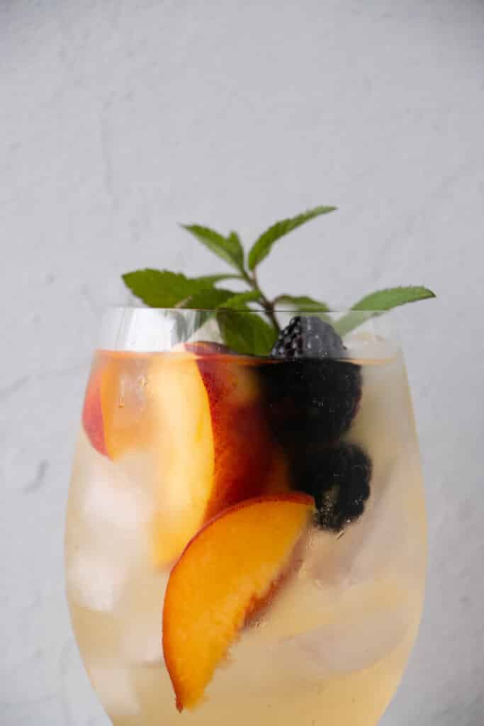 stemless wine glasses filled with ice, a white wine based sangria, peaches, blackberries and a bright green fresh mint stem. 