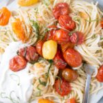Summer Tomato Pasta with a fork running through noodles on the right side of a flat plate.