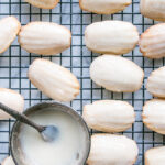 Eggnog Madeleines on a cooling rack with a bright eggnog icing topping.