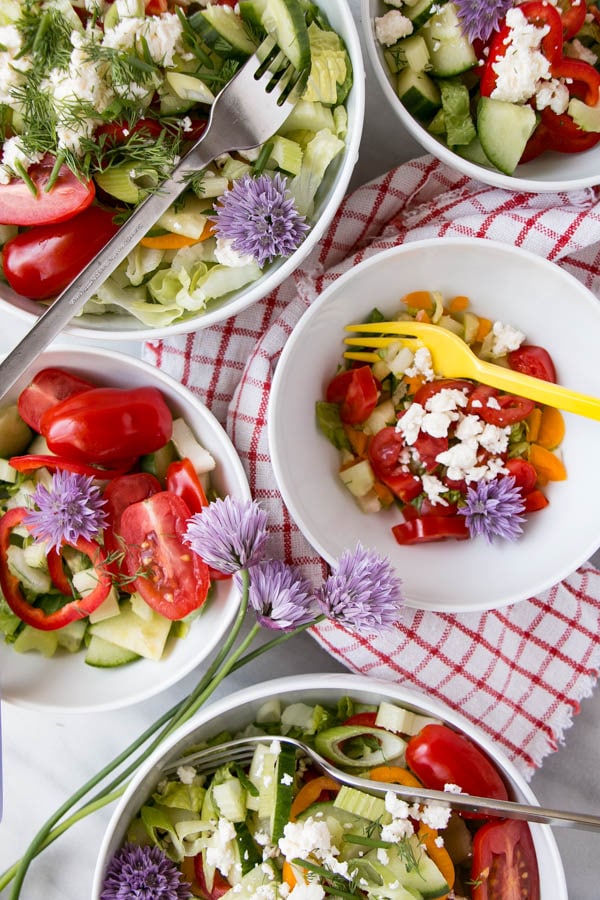 Side Salad recipe with lots of colourful chopped vegetables (lettuce, tomatoes, peppers, cucumbers, etc.) in white bowls with red and white tea towel