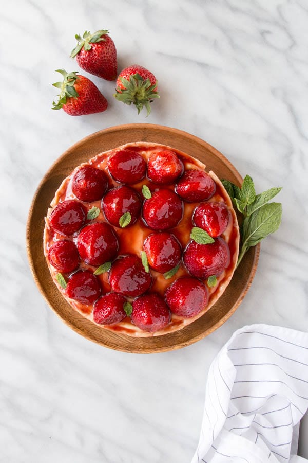 French strawberry tart on a round wooden serving platter.