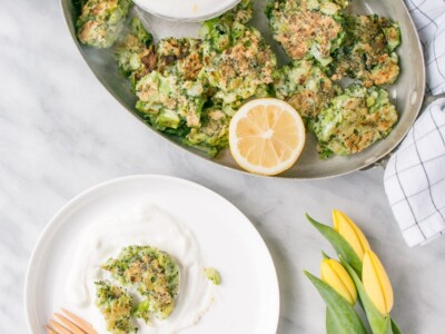 broccoli fritters in serving dish, one on a plate with yogurt dip and yellow flowers