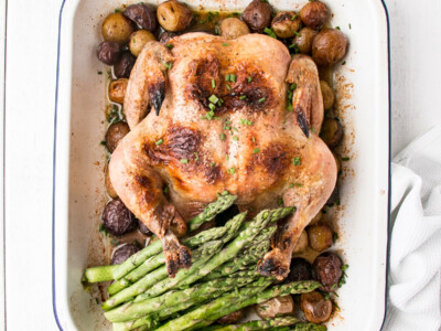 whole roasted chicken, potatoes and asparagus in a white baking dish