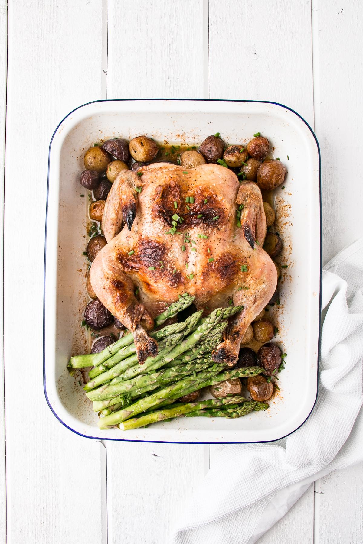 whole roasted chicken, potatoes and asparagus in a white baking dish