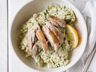 Broccoli and Goat's Cheese Orzo with chicken sliced on top in a white bowl.