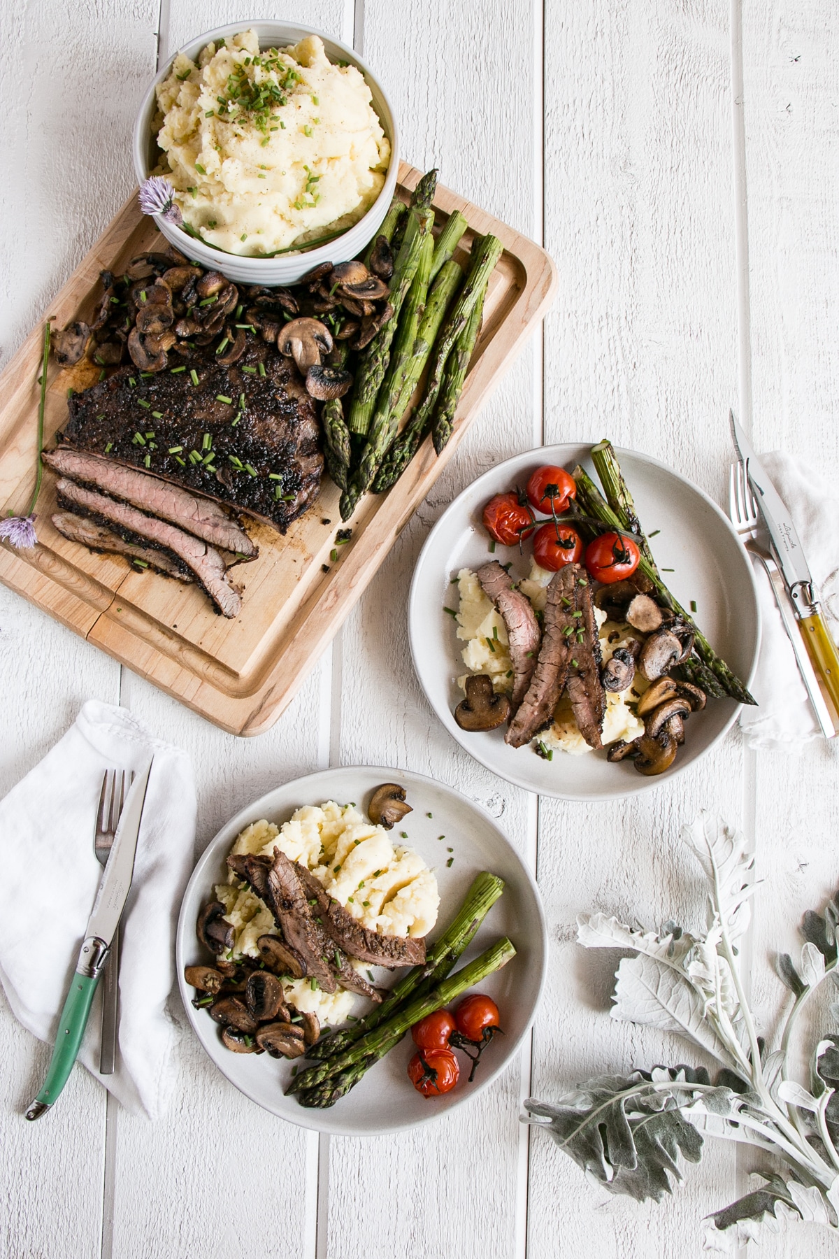 Porcini Rubbed Flank Steak on a white plate with mushrooms, asparagus and grilled cherry tomatoes