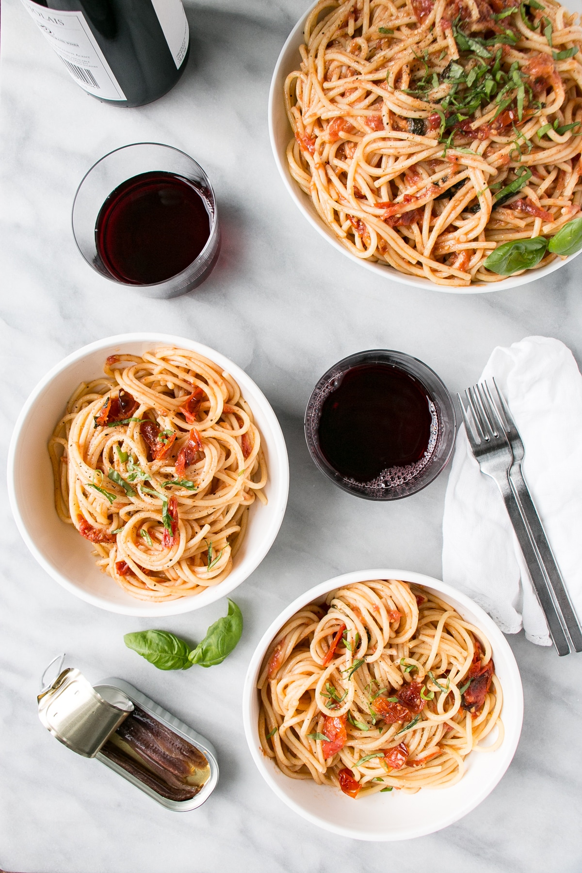 Anchovy and Tomato Pasta in a white bowl with red wine and white linen.