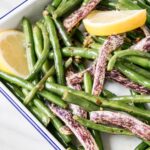 Garlicky Green Beans up close with lemon segements in a white serving tray.