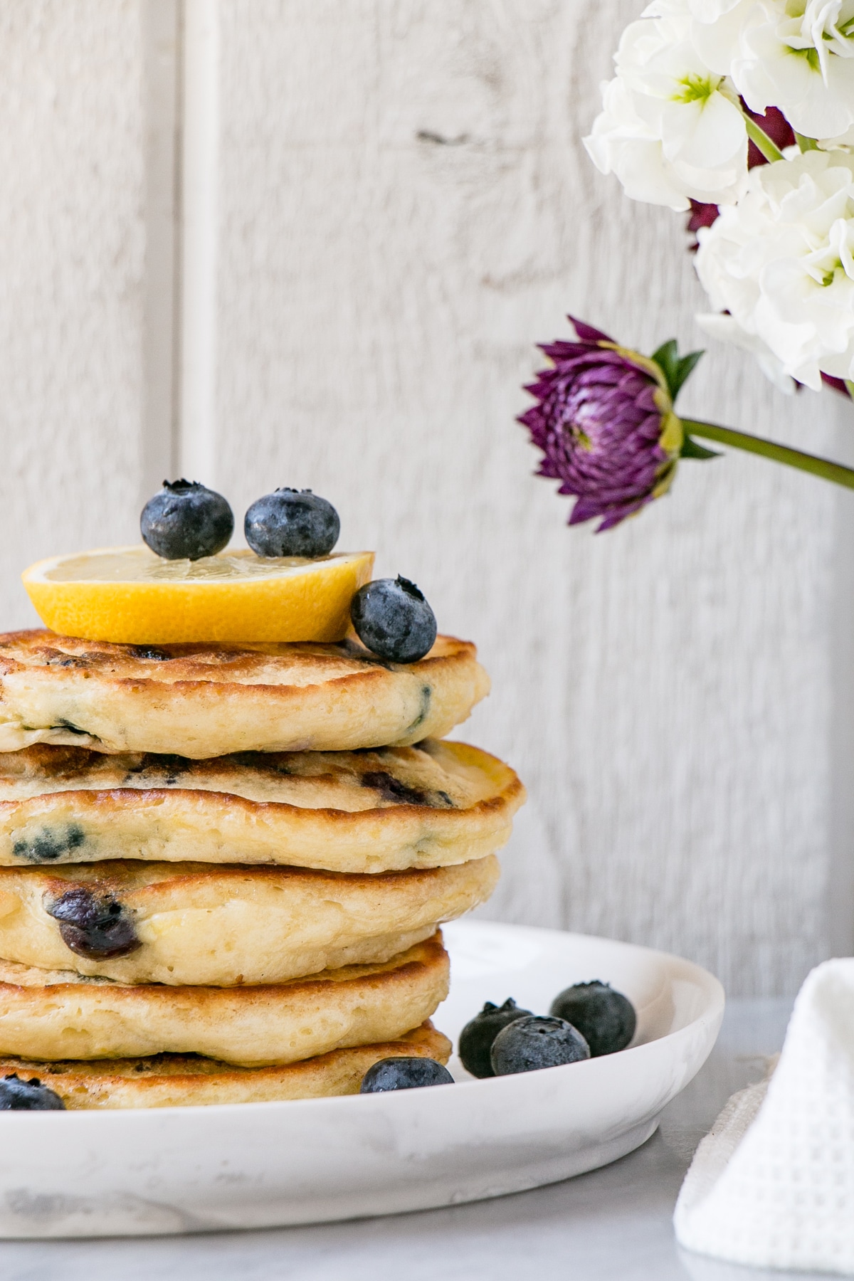 Fluffy Lemon Blueberry Pancakes in a stack with blueberries on a white plate.