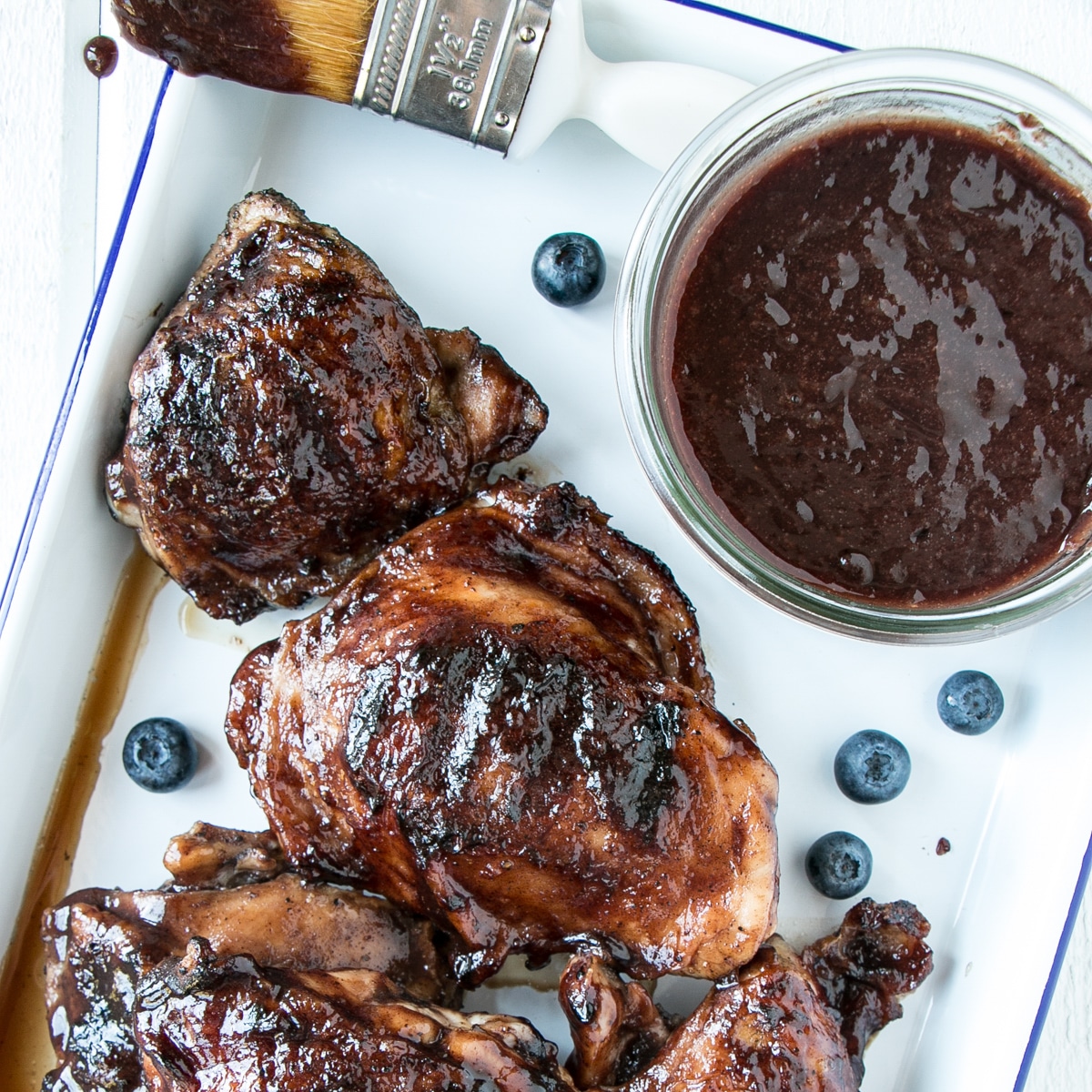 Slow Cooker Blueberry BBQ Sauce on grilled chicken thighs and some sauce in a jar off to the side.