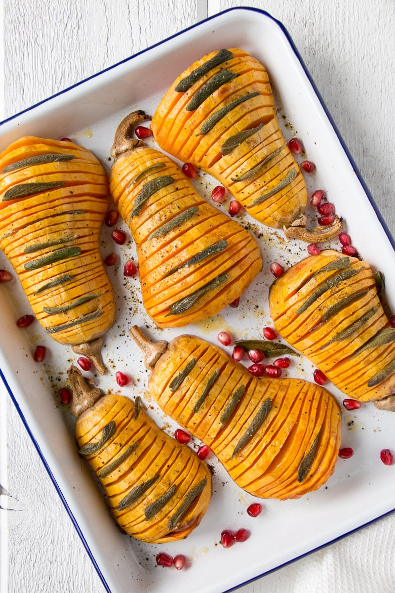 Hassleback Butternut Squash on a white serving tray with sage and pomegranate seeds