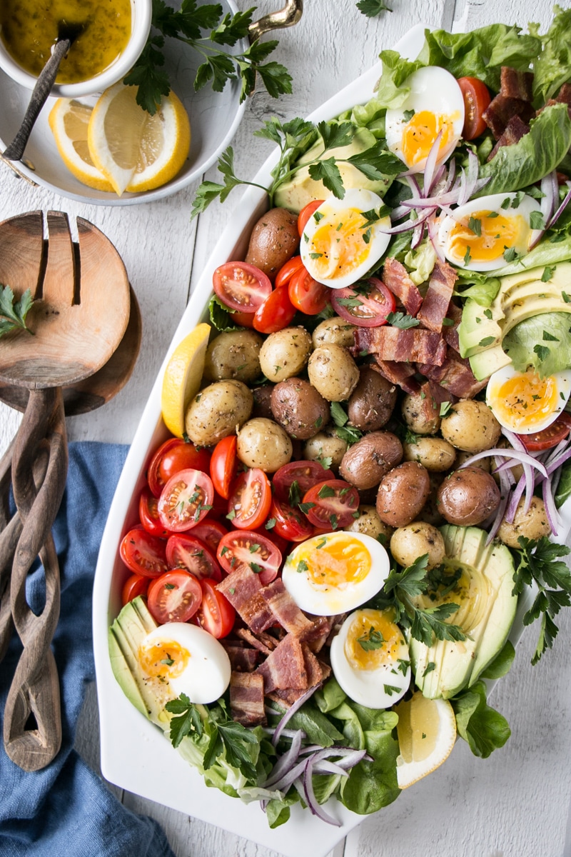 Potato Cobb Salad on a white plate with wooden salad spoons