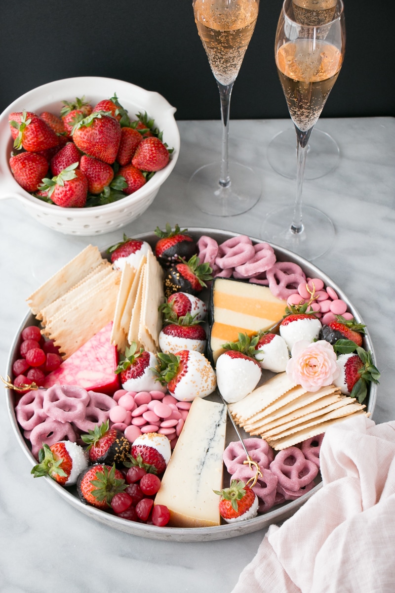 Bright and colourful dessert board with white chocolate and dark chocolate covered strawberries and colourful cheeses.