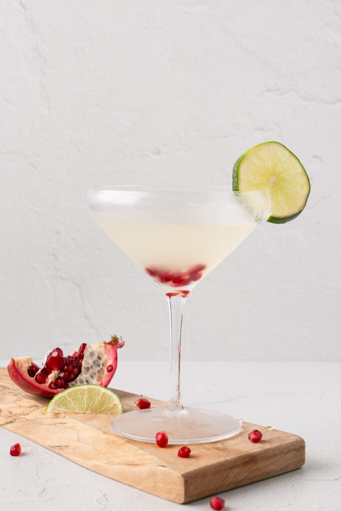 Lime Gimlet with a lime slice on the rim of a chilled martini glass and pomegranate seeds at the bottom of the glass.
