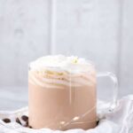 Creamy and decadent Hot White Russian topped with whipped cream in a clear glass mug.