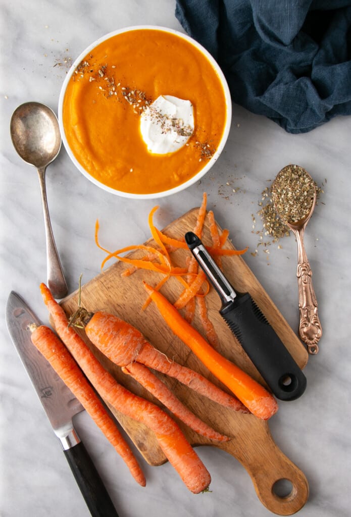 Roasted Carrot Soup in a white bowl with various carrots in the preparation process.