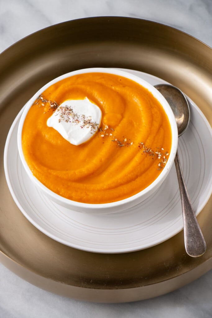 Roasted Carrot Soup in a white bowl with a decorative place setting