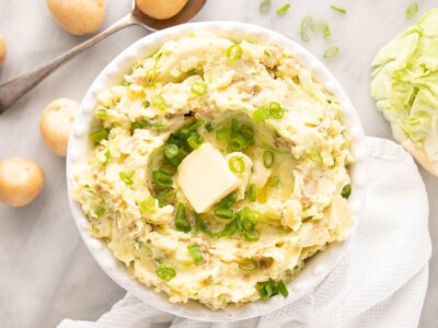 Colcannon with a pat of butter and sliced green onions in a white dish.