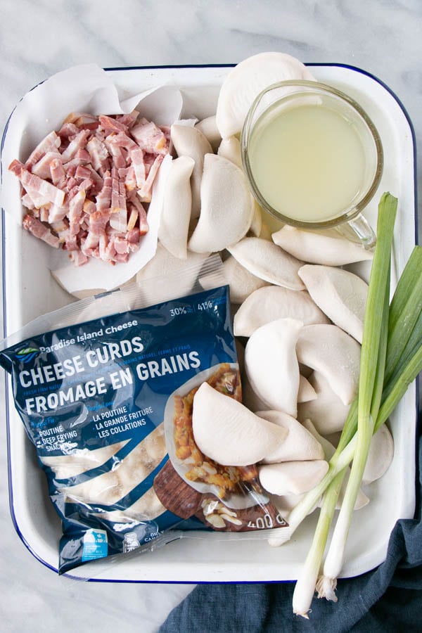 Ingredient prep of frozen pierogis, cheese curds, bacon and green onion for this casserole recipe.