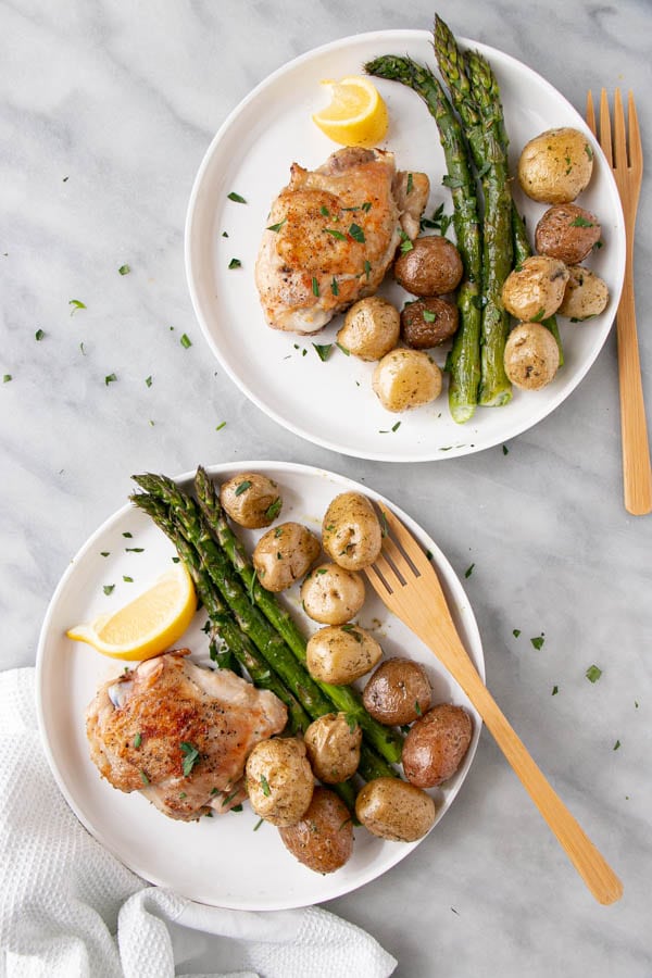 Roasted Potatoes and Asparagus with a seared chicken thigh on a white plate.