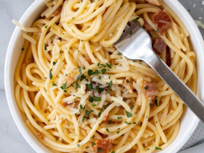 Spaghetti Carbonara twirled around a fork in a white bowl.