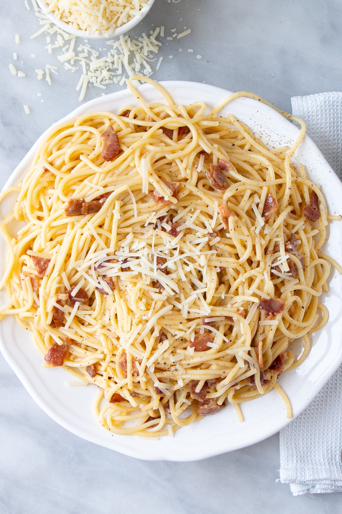 Spaghetti Carbonara with parmesan cheese sprinkled on top on a white serving plate.