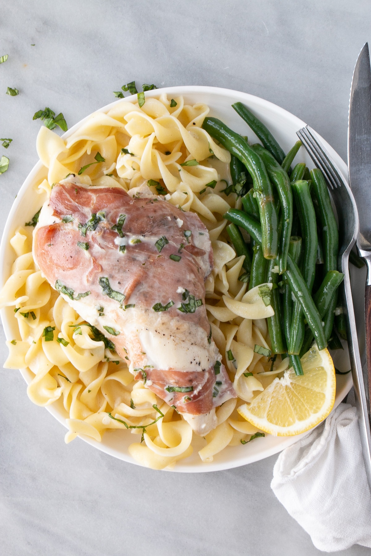 Prosciutto-Wrapped Chicken on top of a bed of broad egg noodles and a side of green beans. 