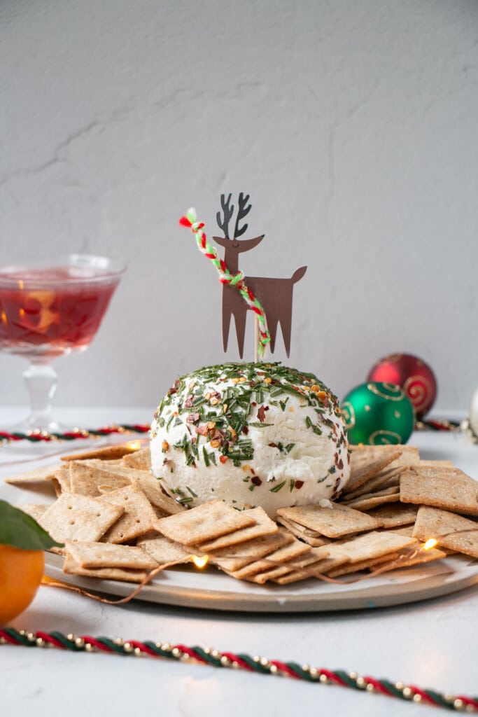 Honey Goat's Cheese Ball recipe with festive drinks and shiny ornaments, surrounding the plate.