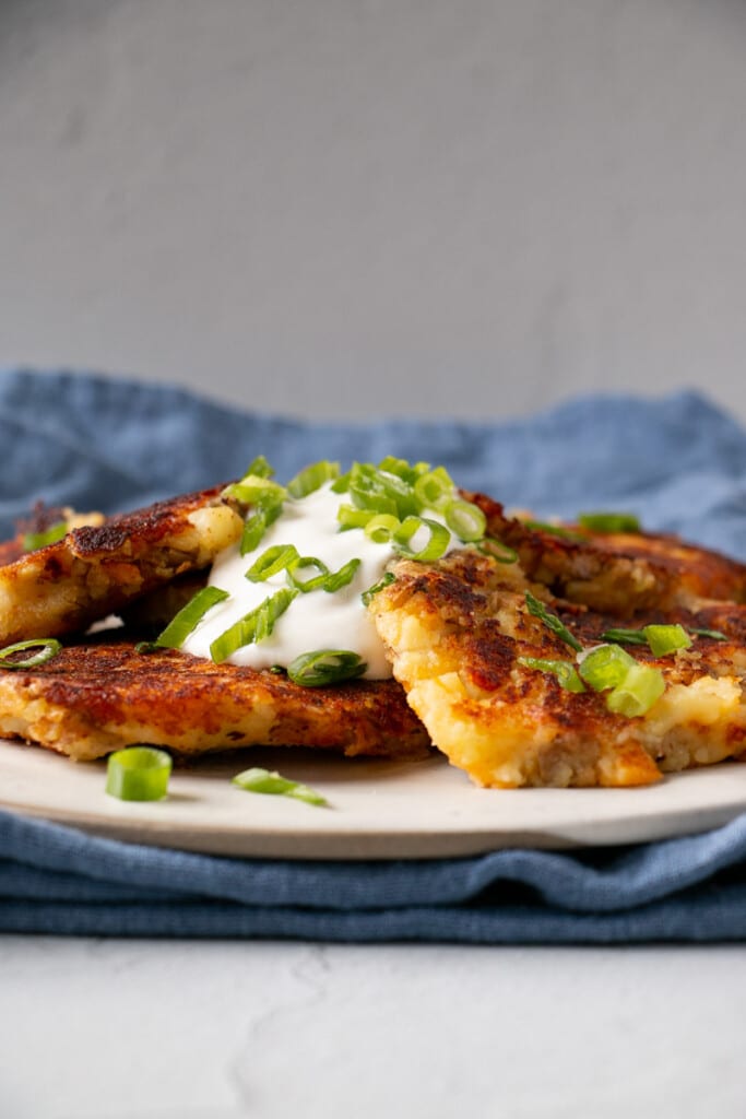 Leftover Crispy golden brown Mashed Potato Pancakes with a big dollop of sour cream and a sprinkling of sliced green onions.