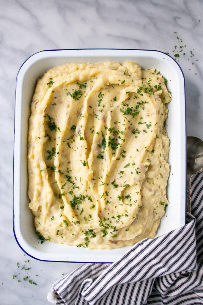 Creamy, pale yellow, mashed potatoes with big curves indented into the potatoes in a shallow white serving tray.