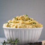 Creamy, piled high Holiday Make Ahead Mashed Potatoes in large white bowl with scattered parsley on top.