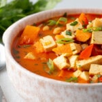 Chickpea and Tofu Coconut Curry Stew piled high into a shallow soup bowl with squeezed lime slices.