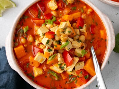 Chickpea and Tofu Coconut Curry Stew piled high into a shallow soup bowl with squeezed lime slices.