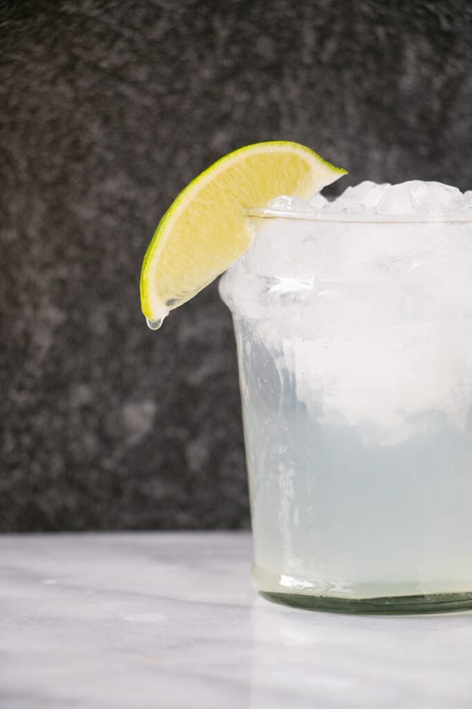 A tall glass with a dripping lime slice on the edge, have filled with crushed ice, tequila, lime juice and mineral water.